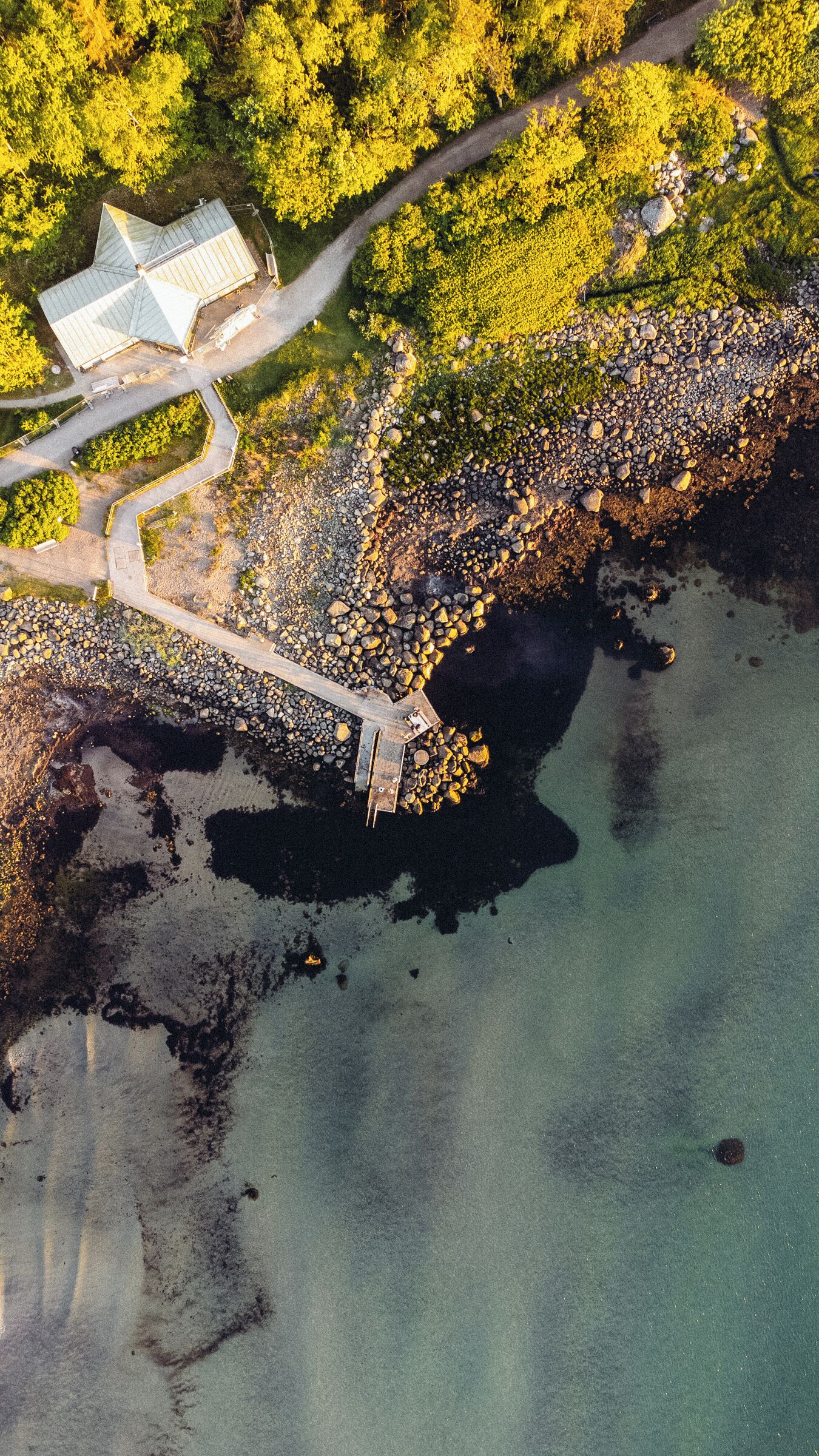 An aerial view of a coastal area with a bridge leading to a building with a green roof.
