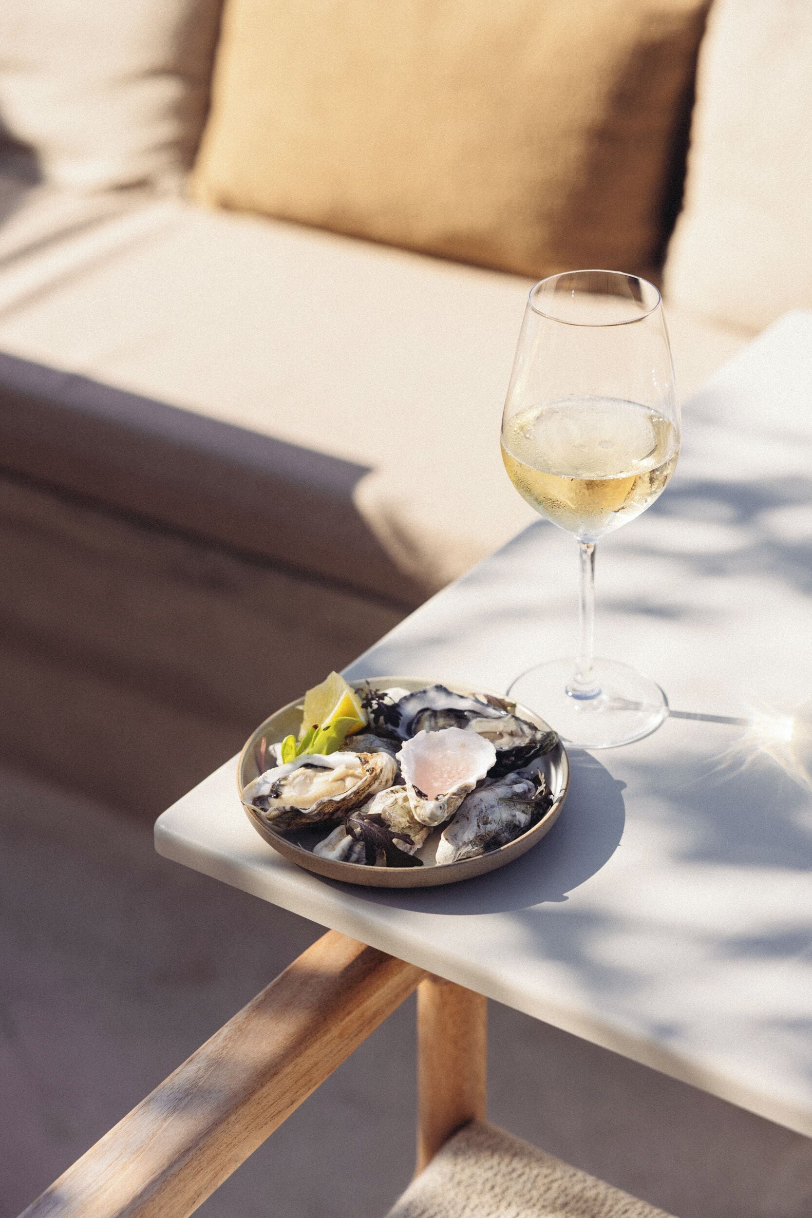 Una mesa de comedor con una fuente de ostras y una copa de vino blanco, en un día soleado.