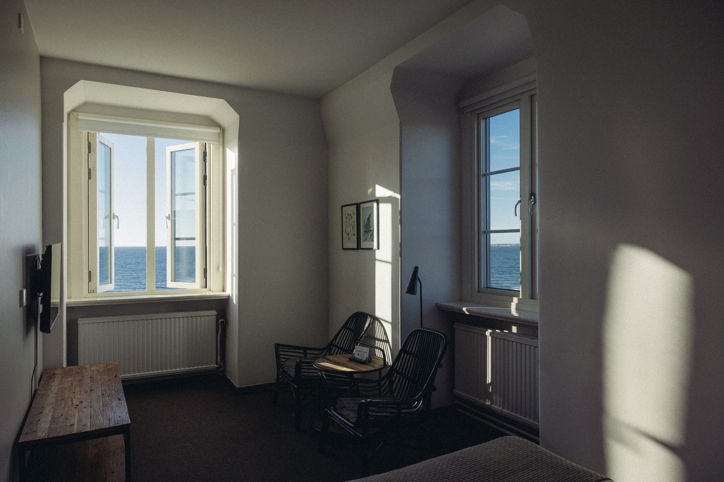 A room with a view of the sea, a wooden table, two black chairs, and a radiator.
