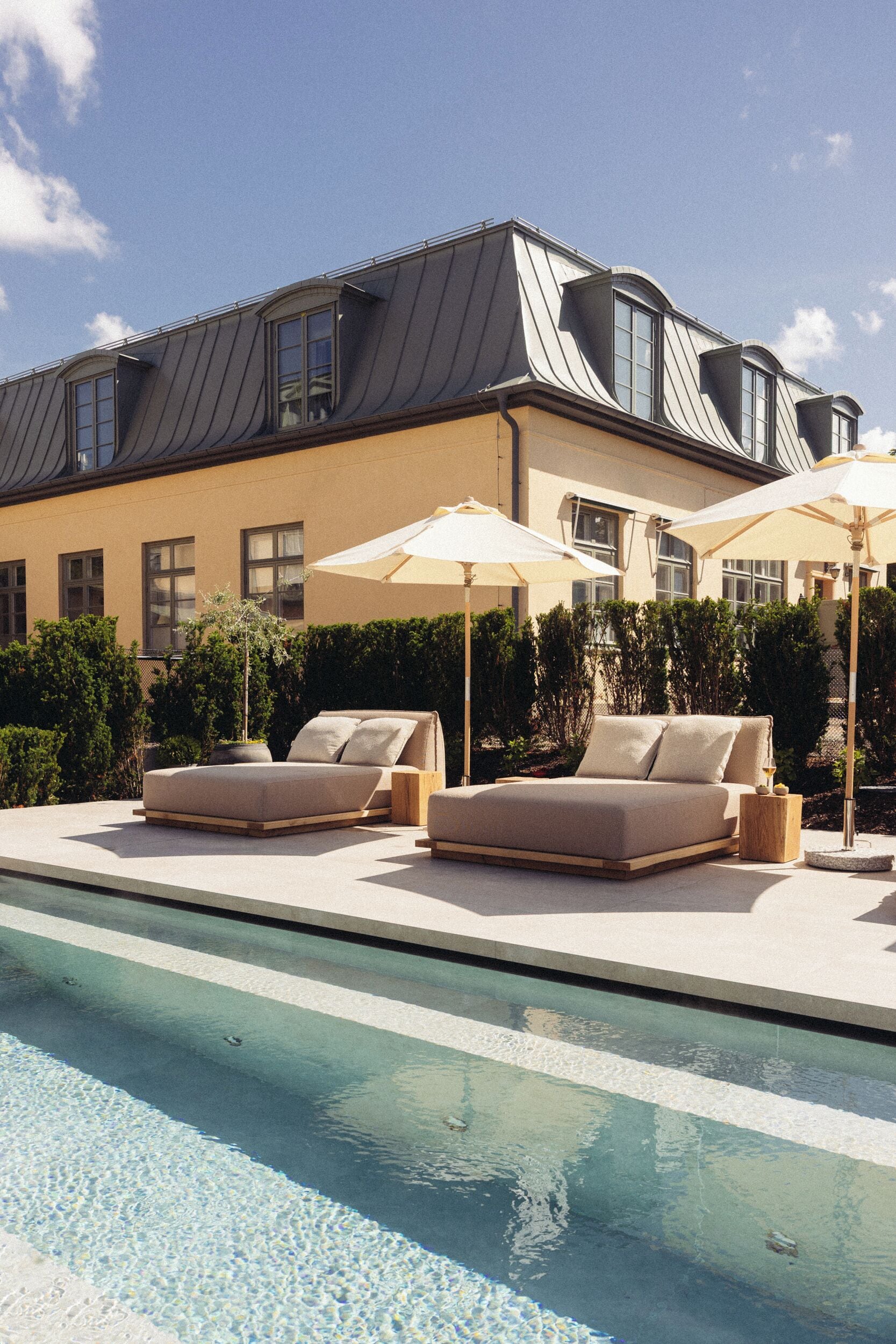 A poolside area with a sofa and two umbrellas, a pool, and a building with a sloped roof.