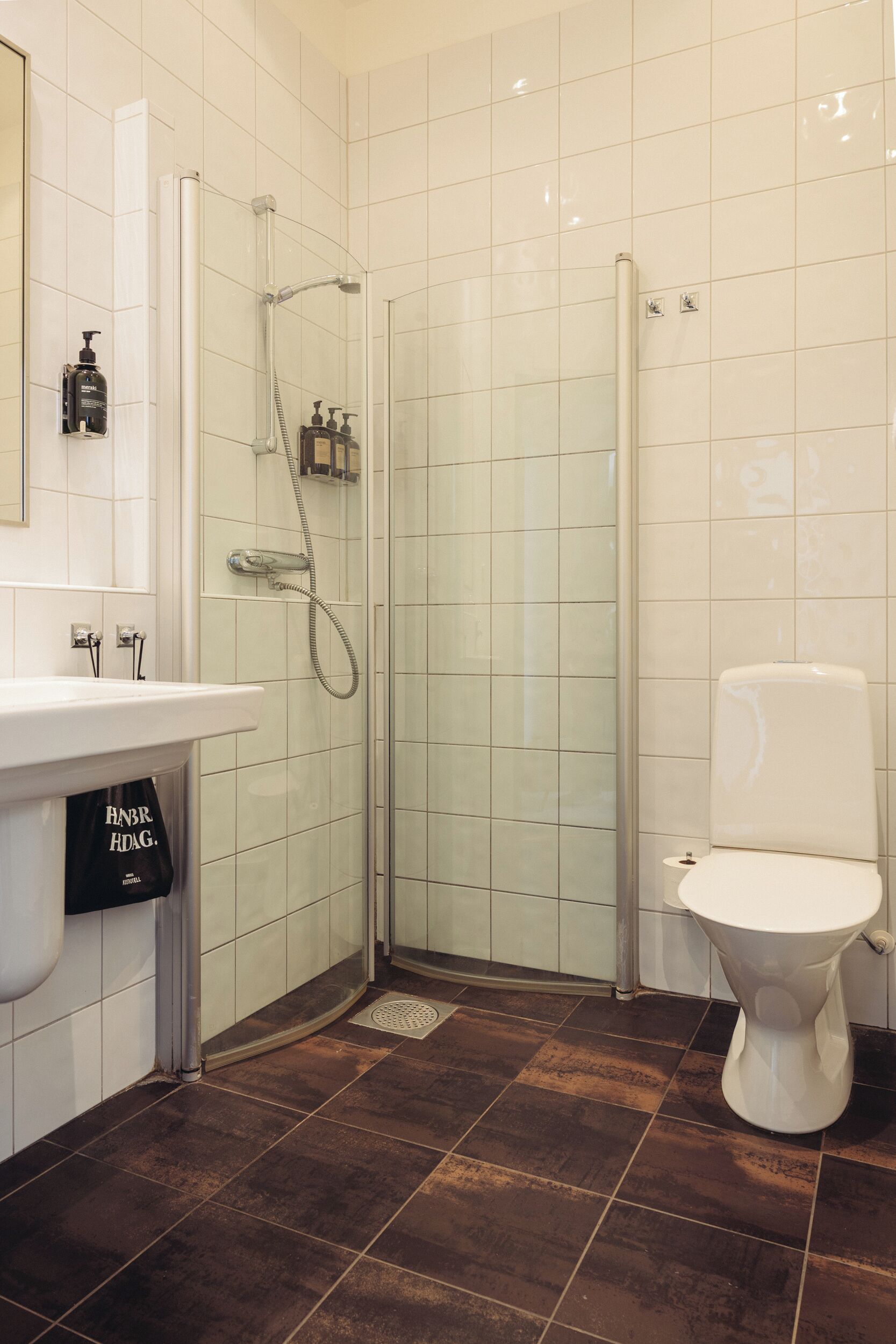 Et badeværelse med bruser, toilet, håndvask og flisebeklædte vægge.