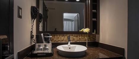 A bathroom with a round sink, a hairdryer, and a coffee machine on the counter.