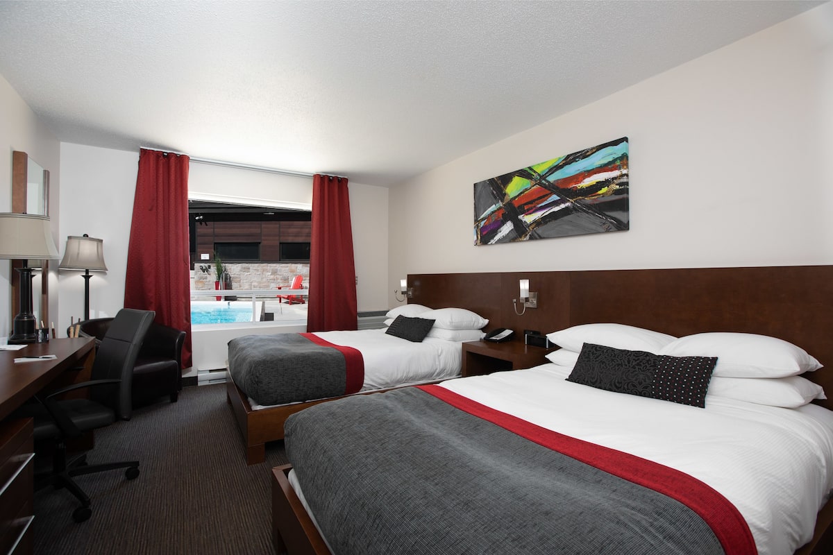 A hotel room with two beds, a desk, a chair, a lamp, and a painting on the wall.