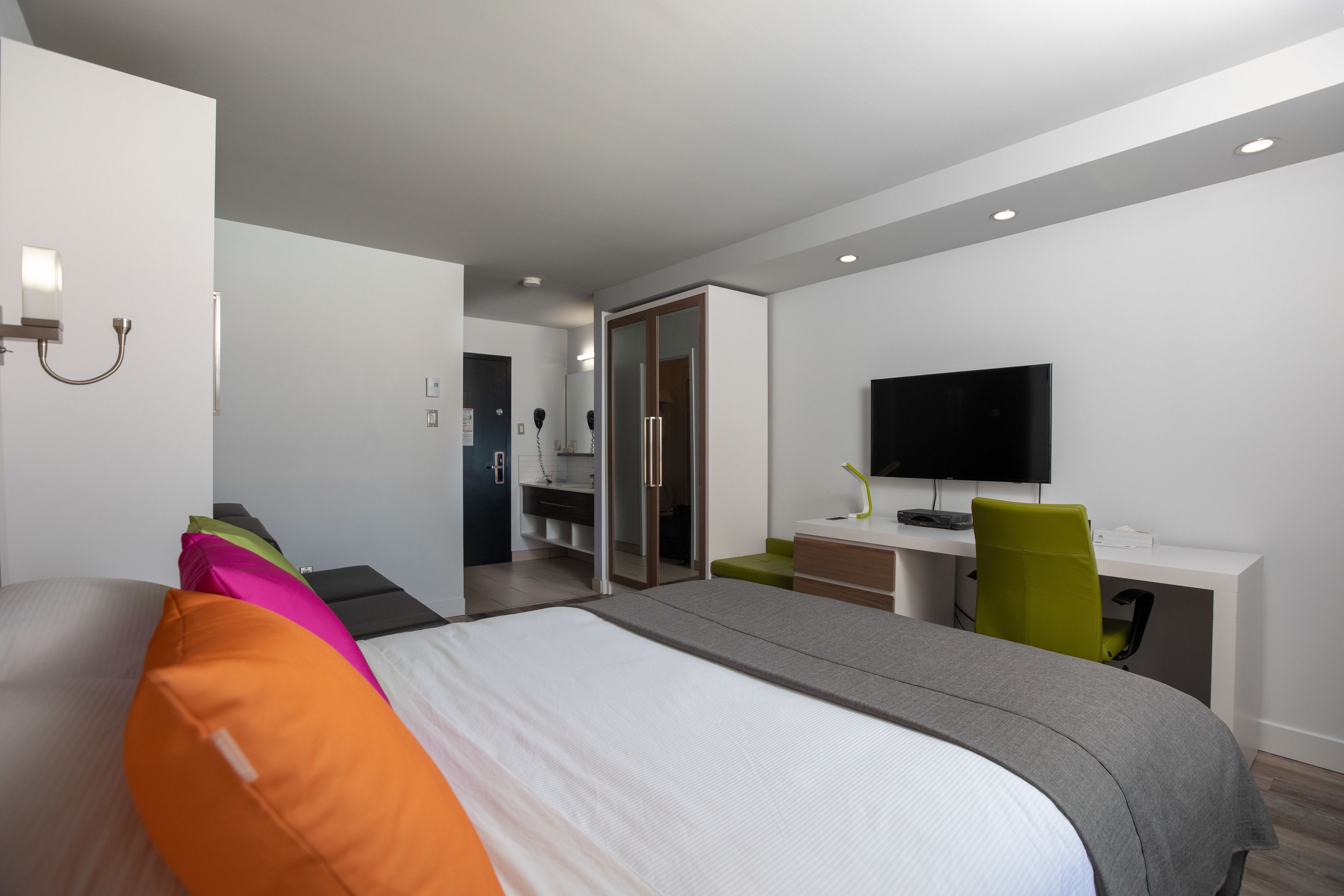 A modern hotel room with a bed, a desk, a chair, and a TV.