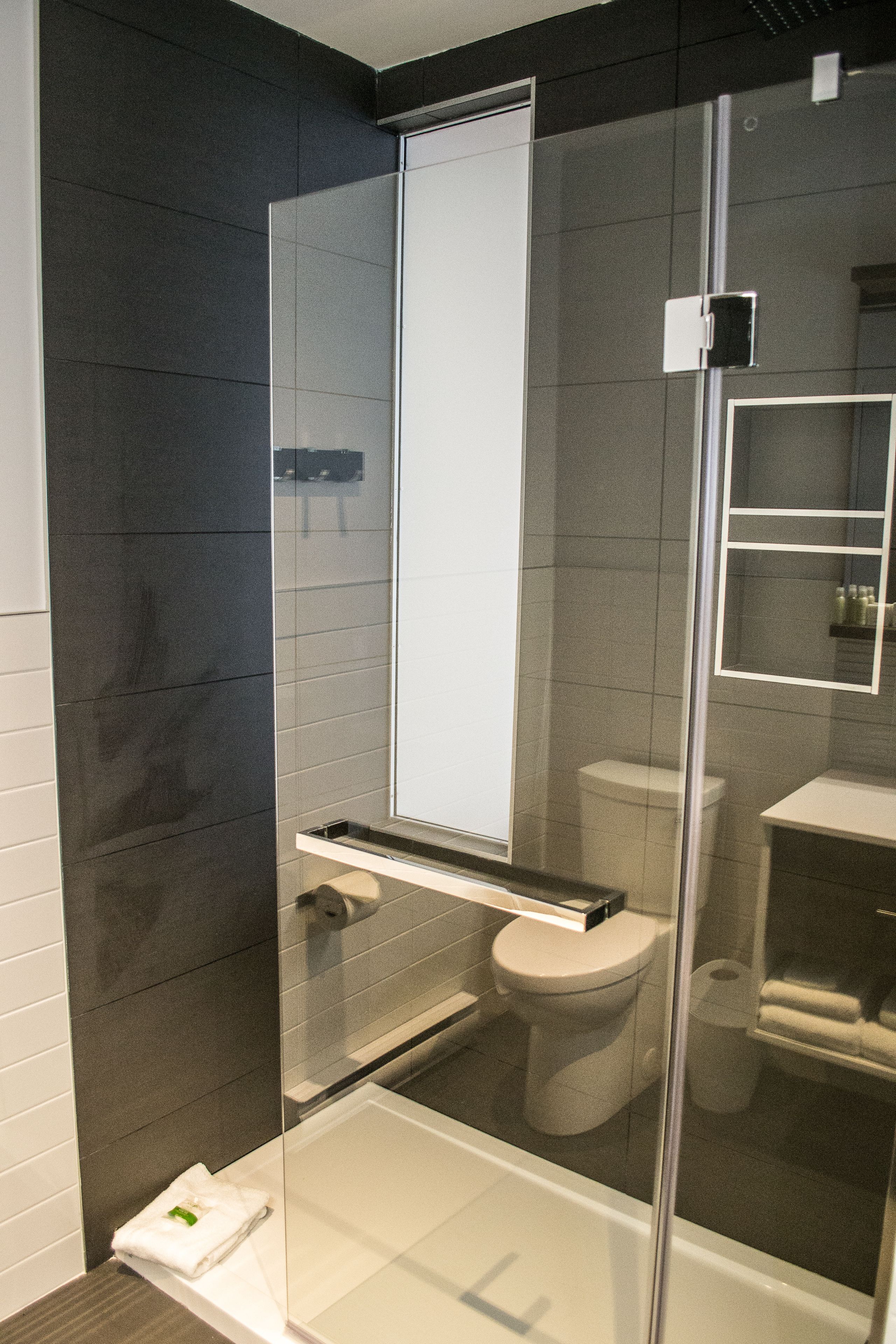 Moderni kylpyhuone, jossa on lasiseinällä varustettu suihku, valkoinen wc-istuin ja valkoinen pesuallas.