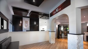 A hotel reception area with a modern design, featuring a reception desk, seating area, and a sign reading "Chez Voûs". - Hotel V (Gatineau)