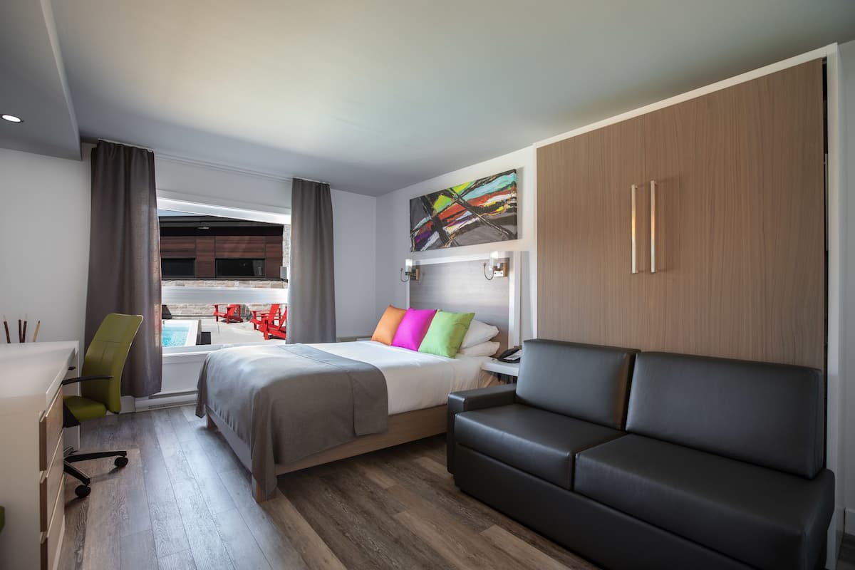 A modern hotel room with a bed, a sofa, a desk, and a view of a pool.