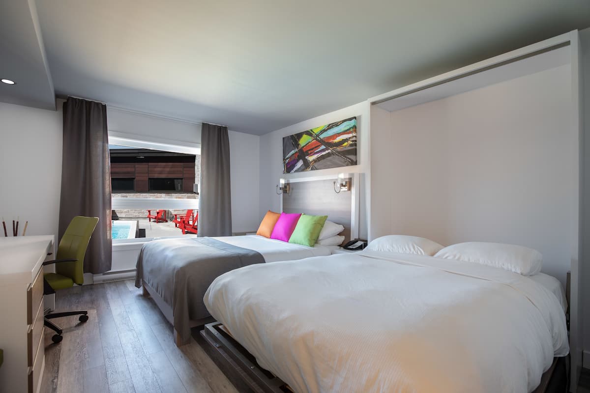 A hotel room with two beds, a desk, a chair, and a view of the pool.