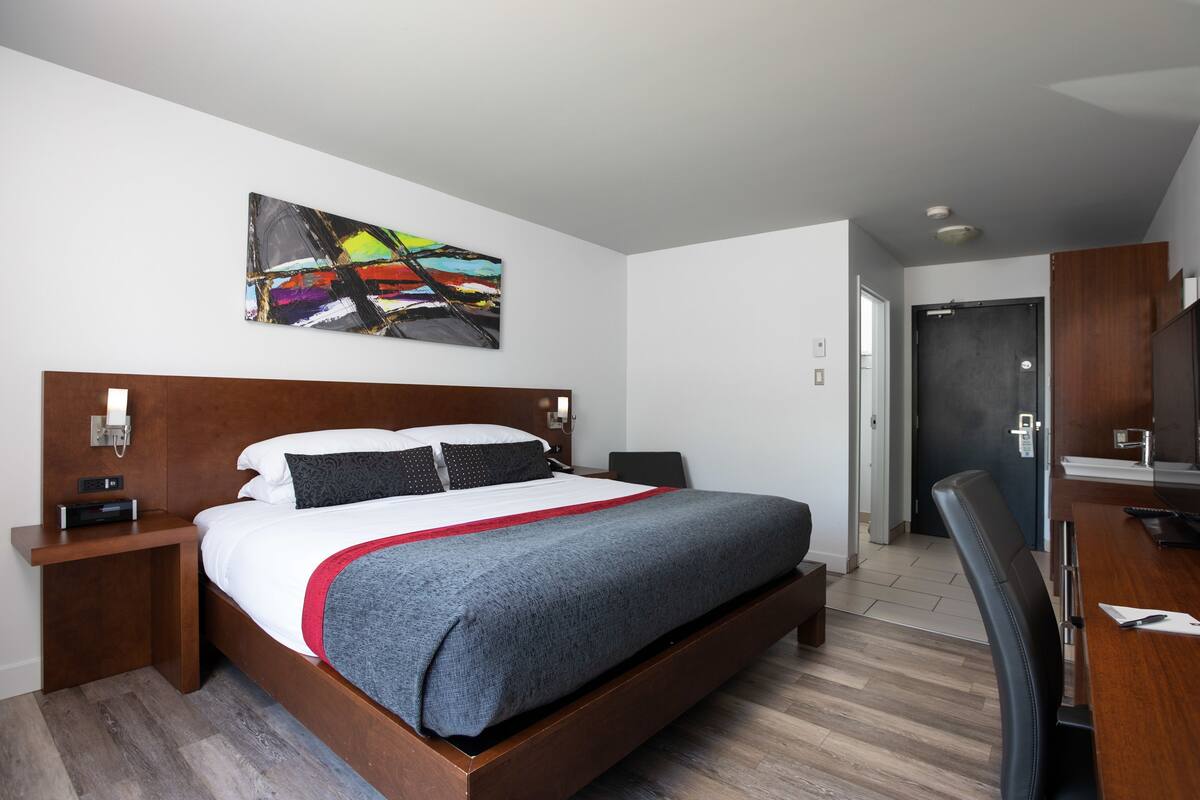 A modern hotel room with a wooden bed, a desk, and a chair.