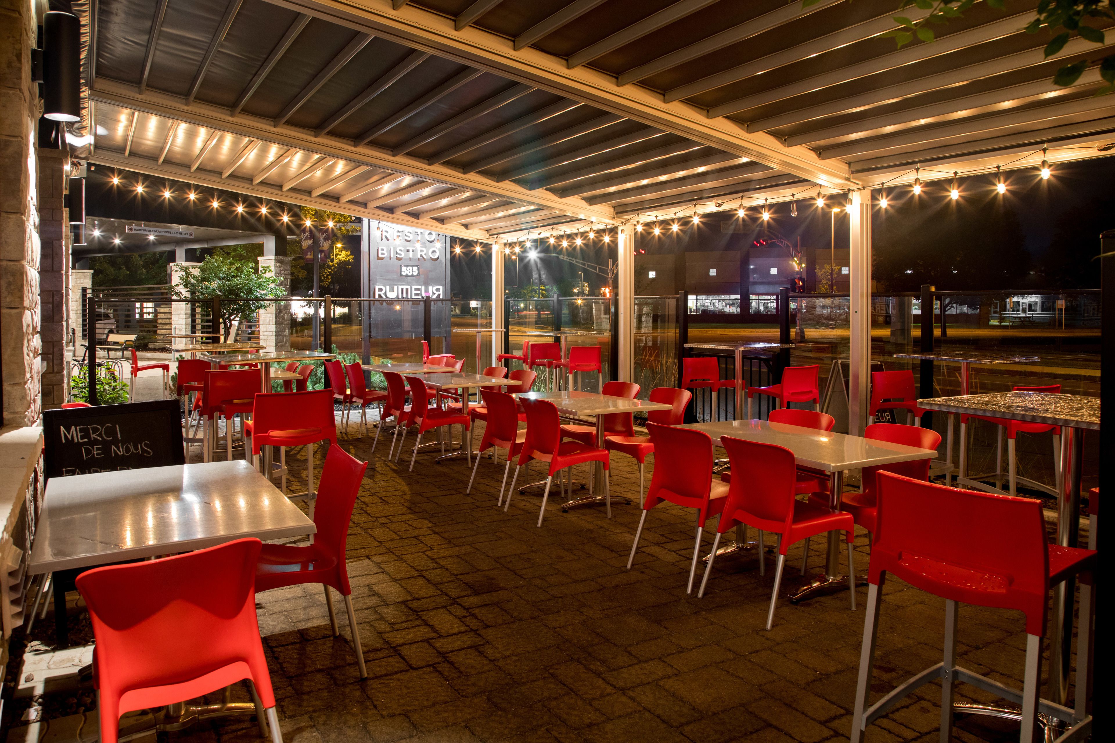 An outdoor café with red chairs and tables, a covered seating area, and string lights.