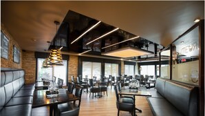 A restaurant with high ceilings, modern lighting, and a mix of booth and table seating. - Hotel V (Gatineau)