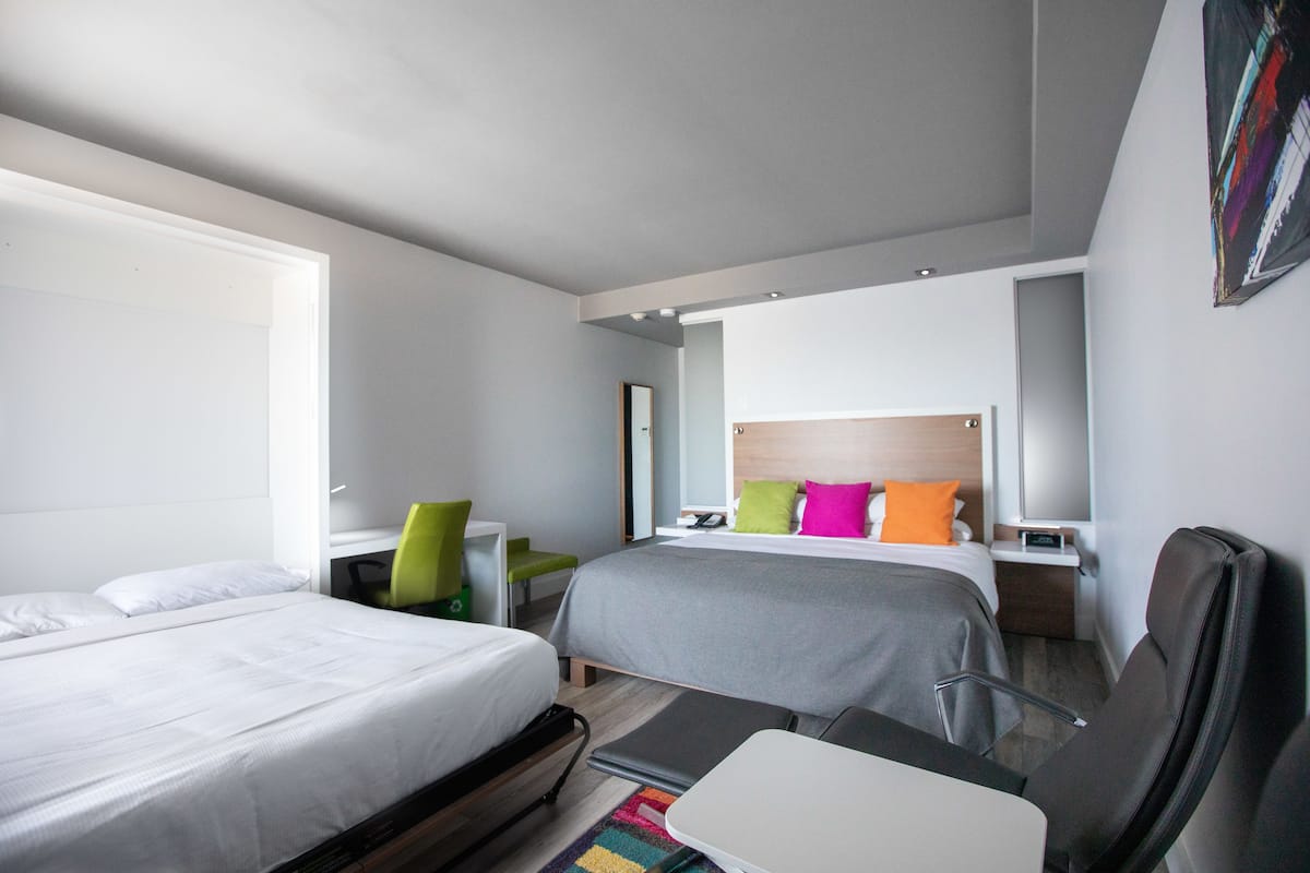 A hotel room with two beds, a desk, a chair, and a small table.