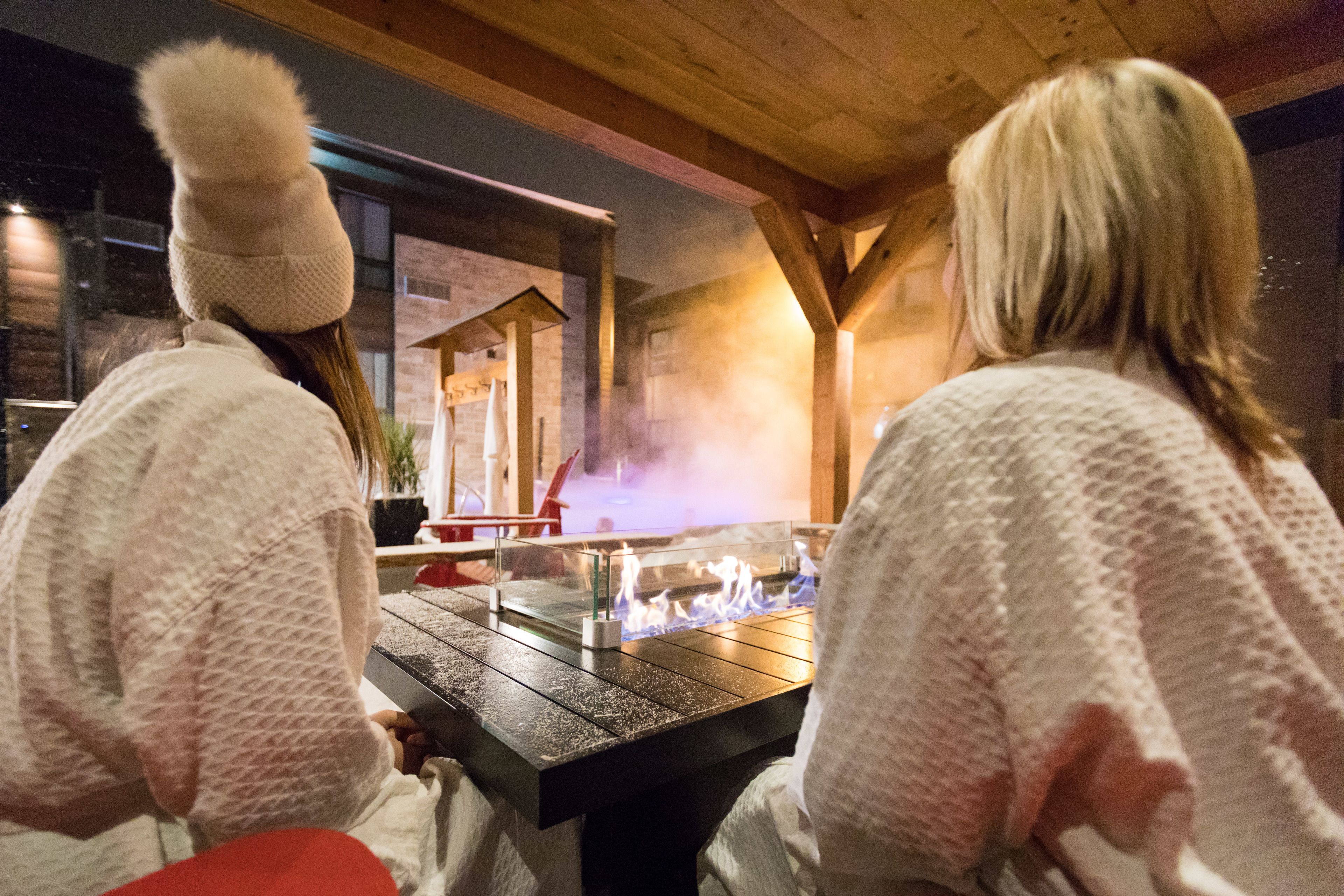 Two people sitting at a table with a glass-top stove, wooden beams, and a brick wall in the background.