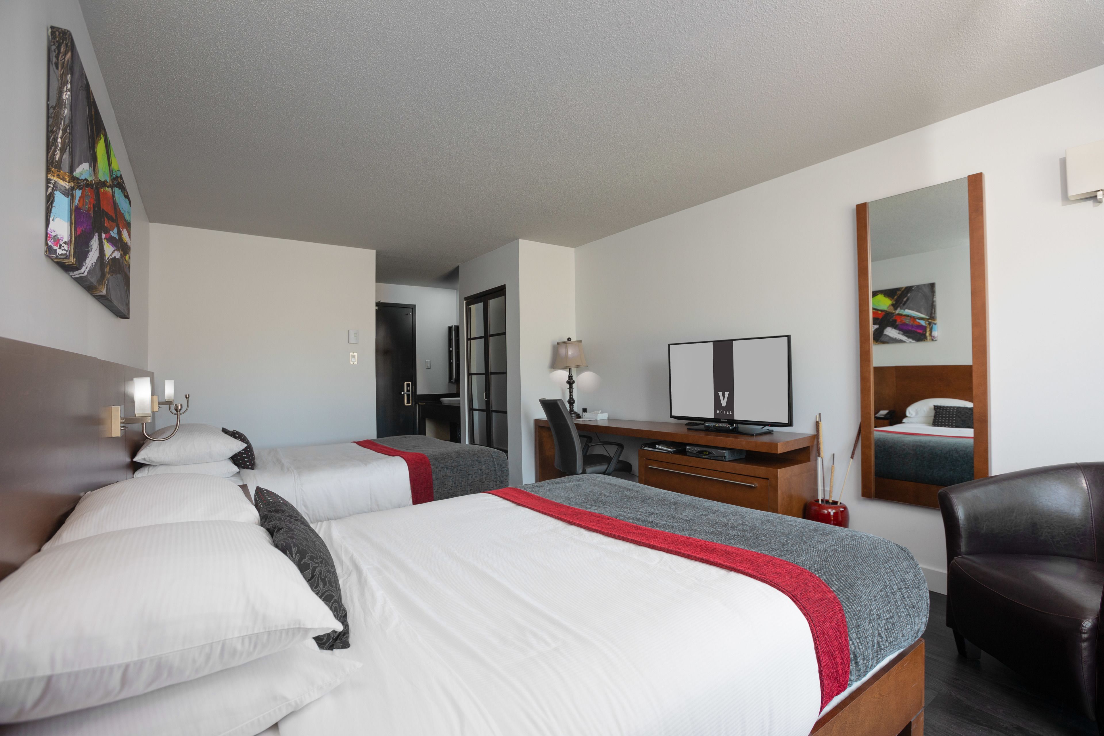 Habitación de hotel con dos camas, un escritorio, una silla, un televisor y un espejo.