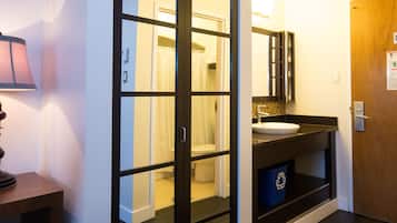 A modern bathroom with a glass door leading to a shower area, a sink with a mirror, and a trash bin.