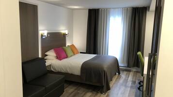A modern hotel room with a bed, a sofa, and a window with curtains.