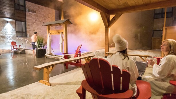 A wooden interior with a stone wall, a bench, and red chairs. - Hotel V (Gatineau)