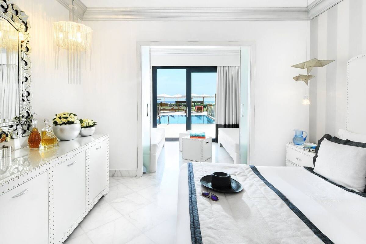A hotel room with a bed, a bedside table, a dresser, a large mirror, and a view of a pool and balcony.