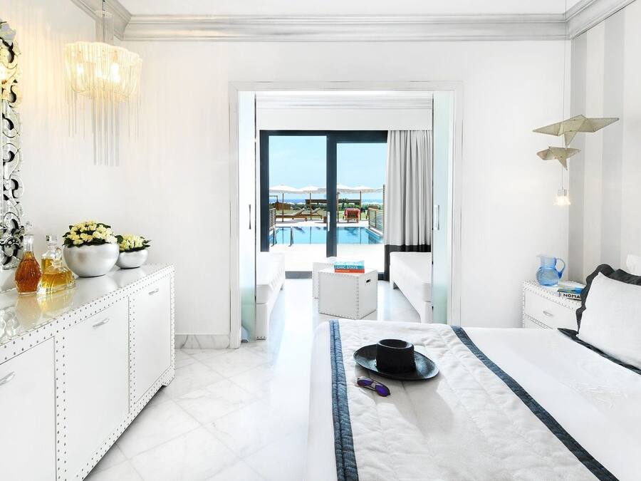 A hotel room with a bed, a bedside table, a dresser, a large mirror, and a view of a pool and balcony.