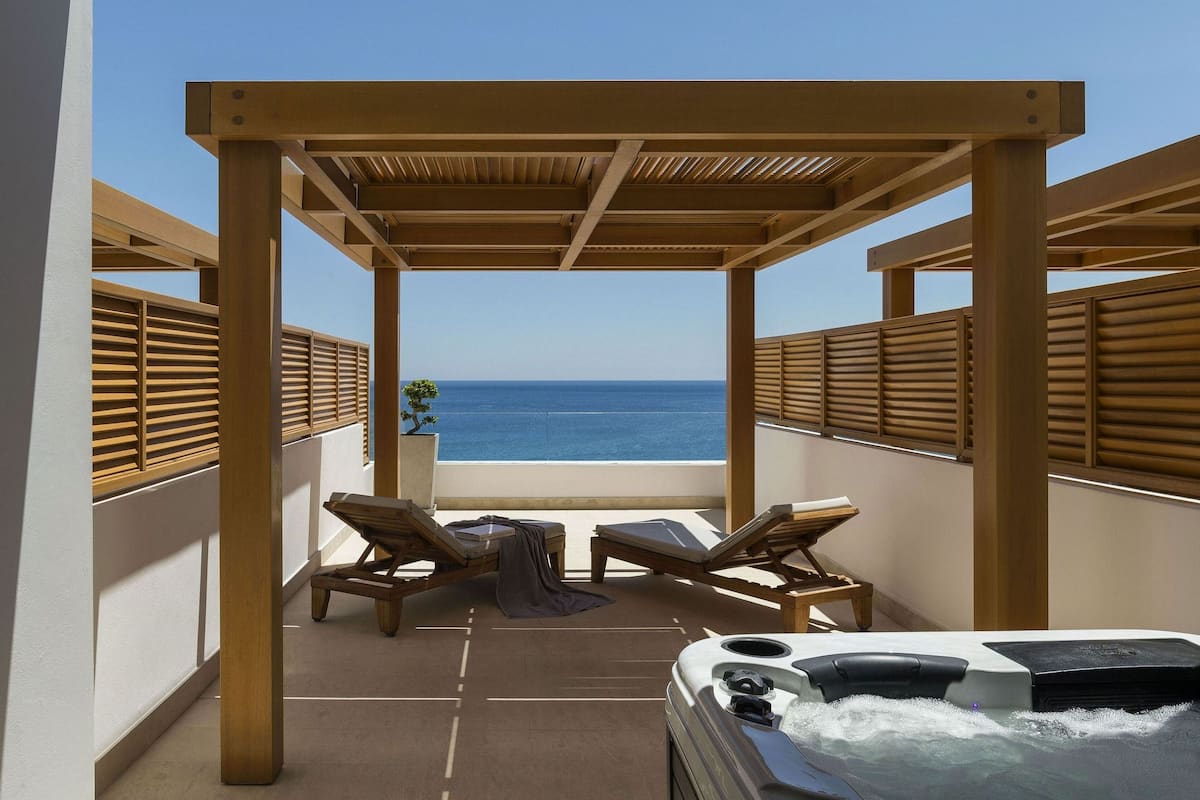 A balcony with wooden railings, two lounge chairs, a small table, and a hot tub.
