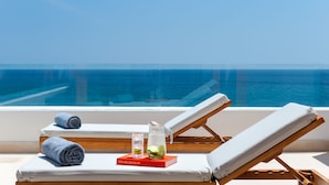Un espace aménagé au bord de la piscine, avec deux chaises longues, un livre intitulé « Le grand livre des Hamptons », une carafe contenant une boisson et un verre d’eau.