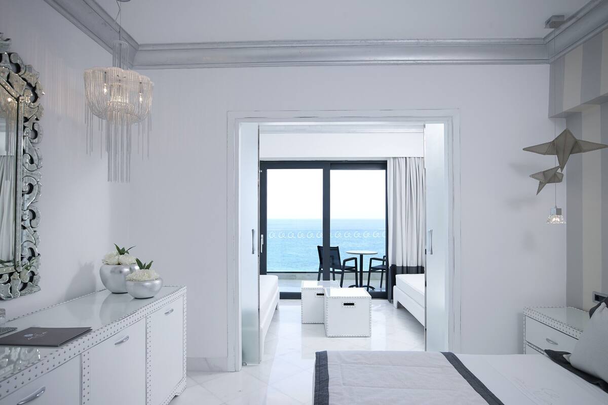 A modern hotel room with a large bed, a desk, and a view of the sea.