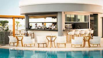 Eine Poolbar mit weißen Korbstühlen, einer Theke und Blick auf das Meer.