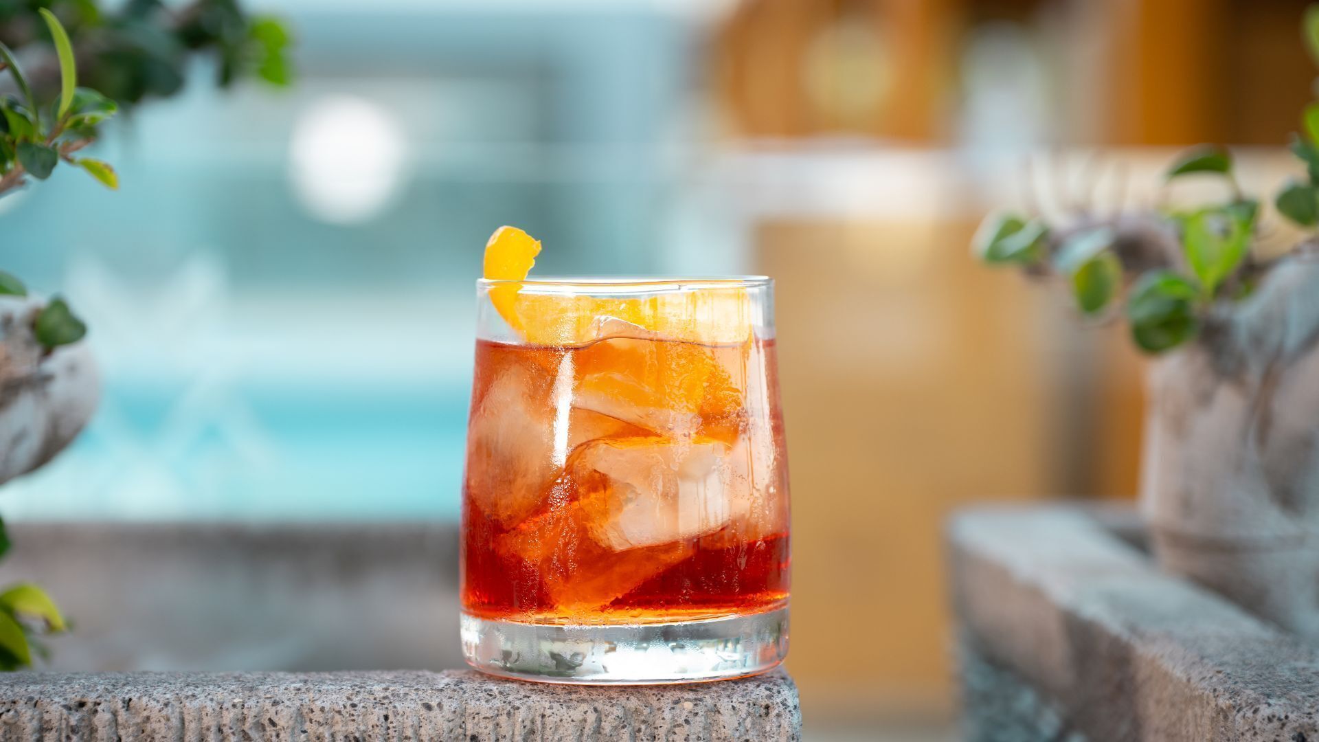 Un vaso de bebida roja con hielo y una rodaja de naranja sobre una superficie de piedra.
