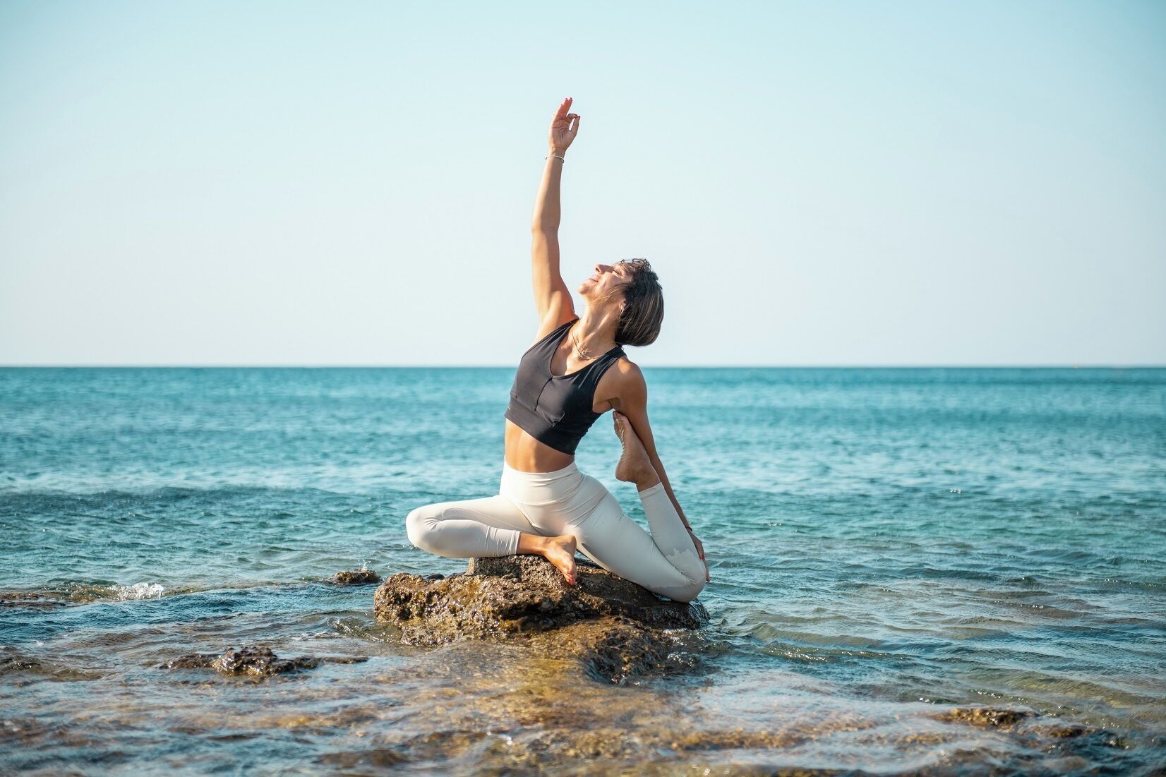 Una persona realizando una postura de yoga sobre un saliente rocoso junto al mar.