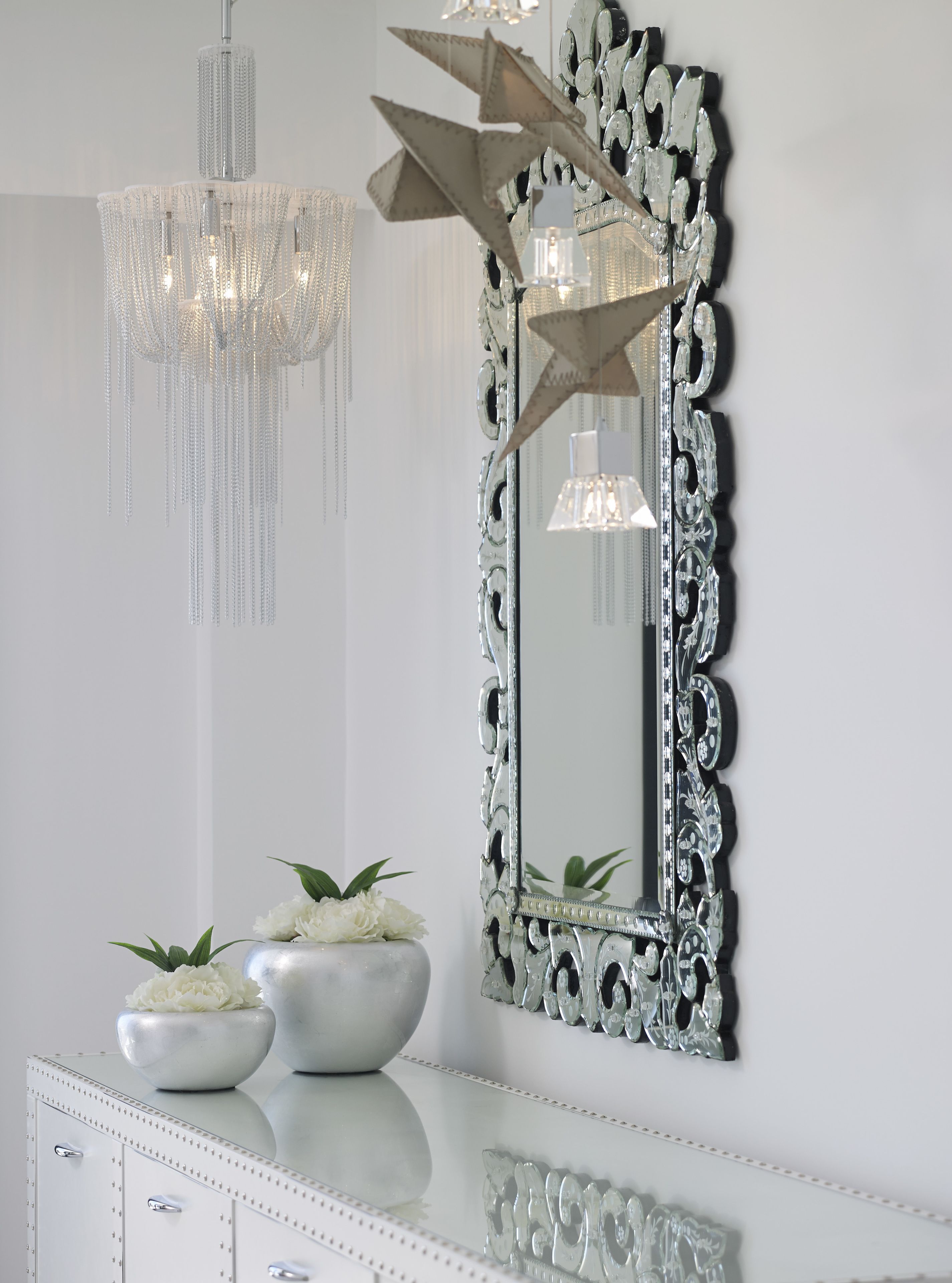 Un miroir avec un cadre orné, deux vases blancs ornés de fleurs et un lustre.