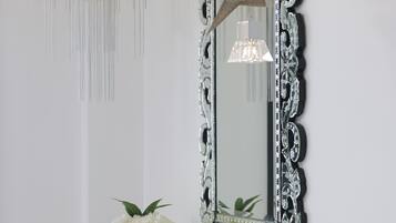 Un miroir avec un cadre orné, deux vases blancs ornés de fleurs et un lustre.
