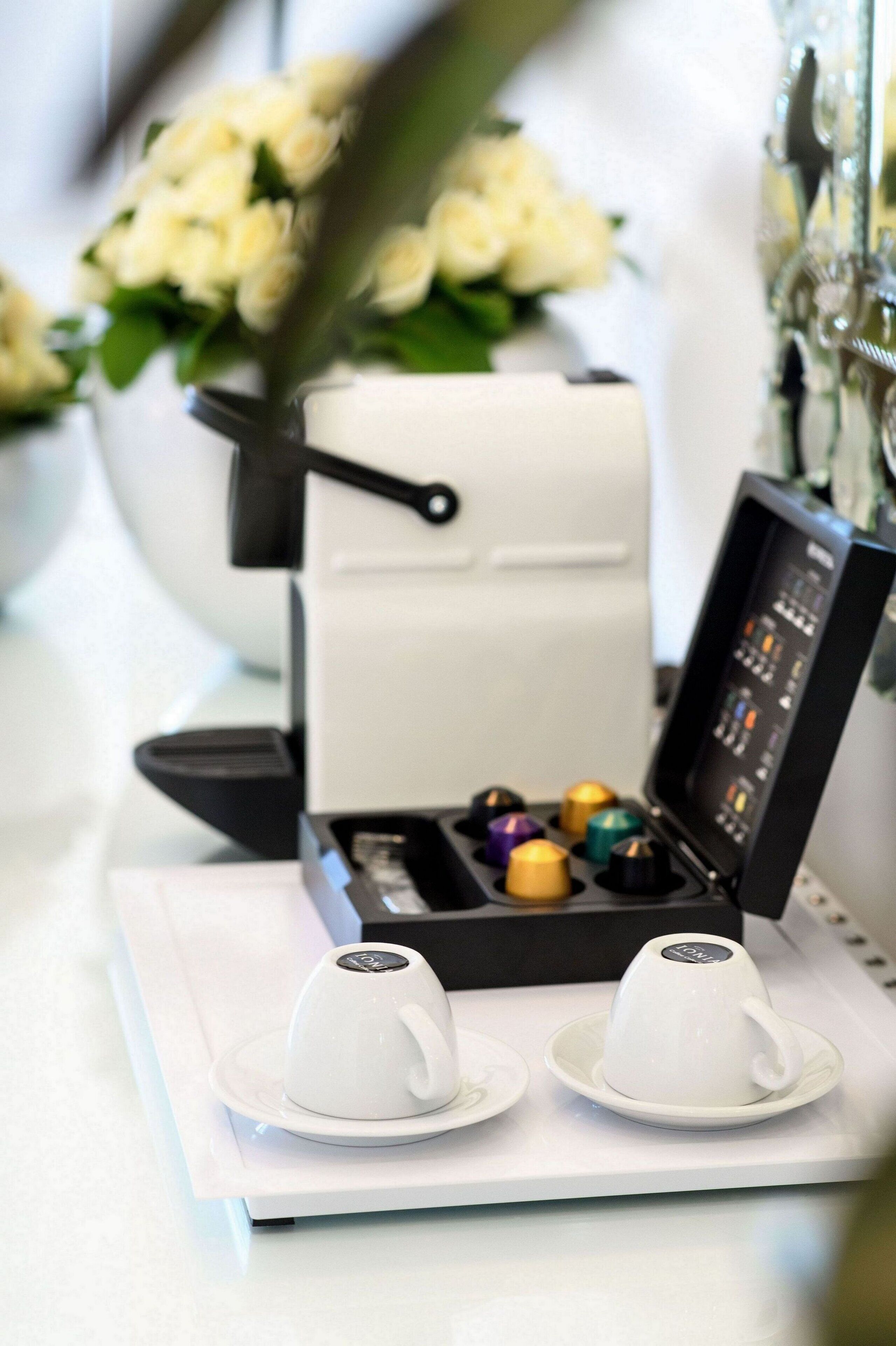 A coffee machine with two cups on a tray, a flower vase, and a wall with a decorative element.