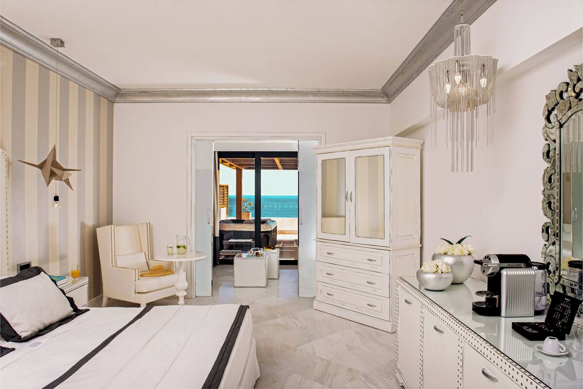 A hotel room with a bed, a desk, a chair, a wardrobe, and a view of the sea.