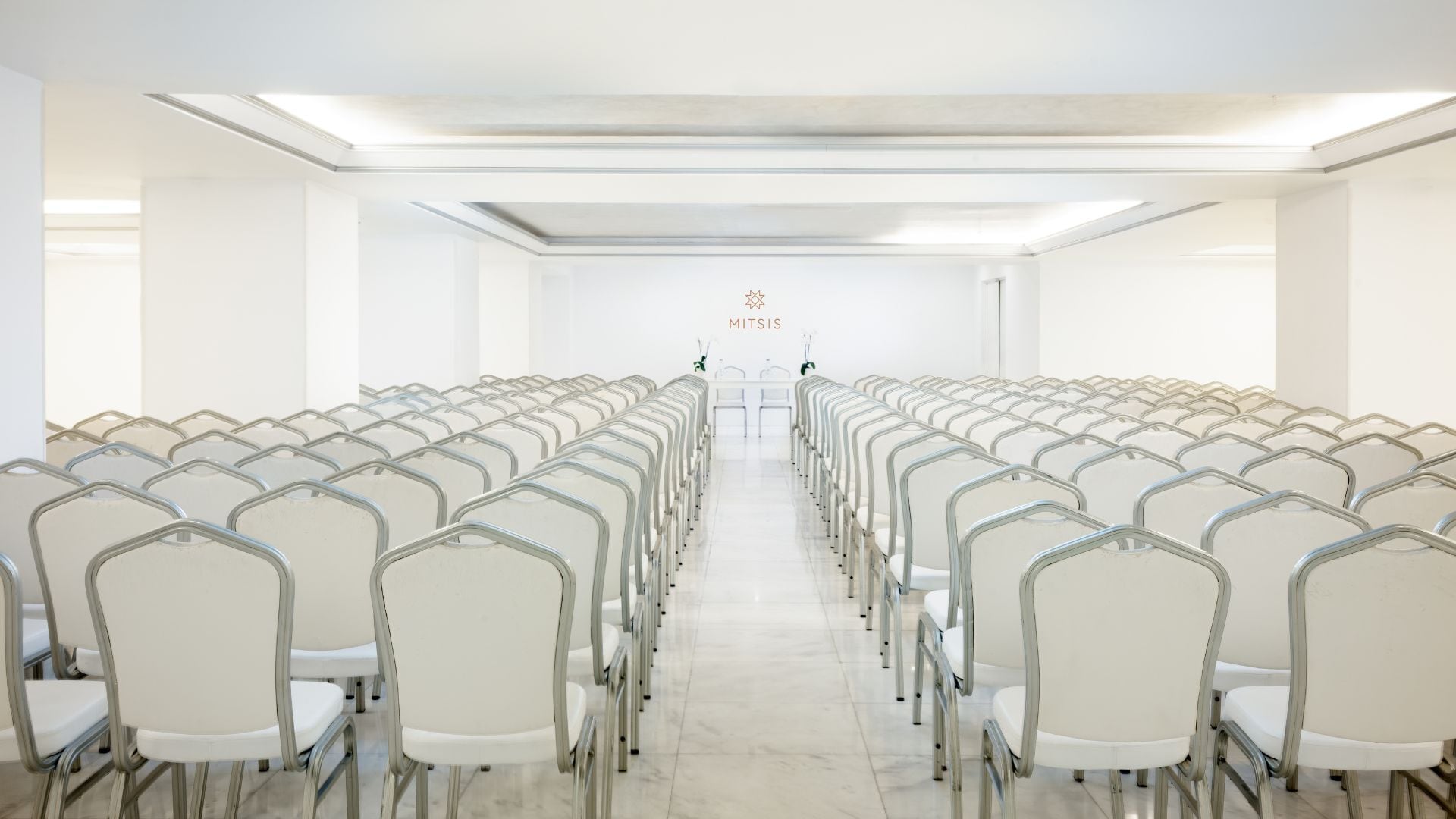 A conference room with rows of white chairs and a central table.