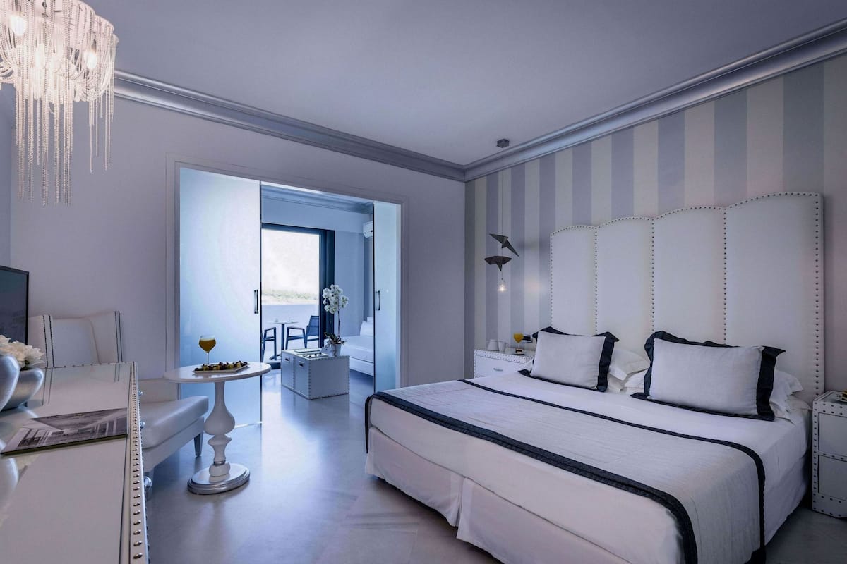 A modern bedroom with a large bed, a chandelier, and a view of the outdoors.