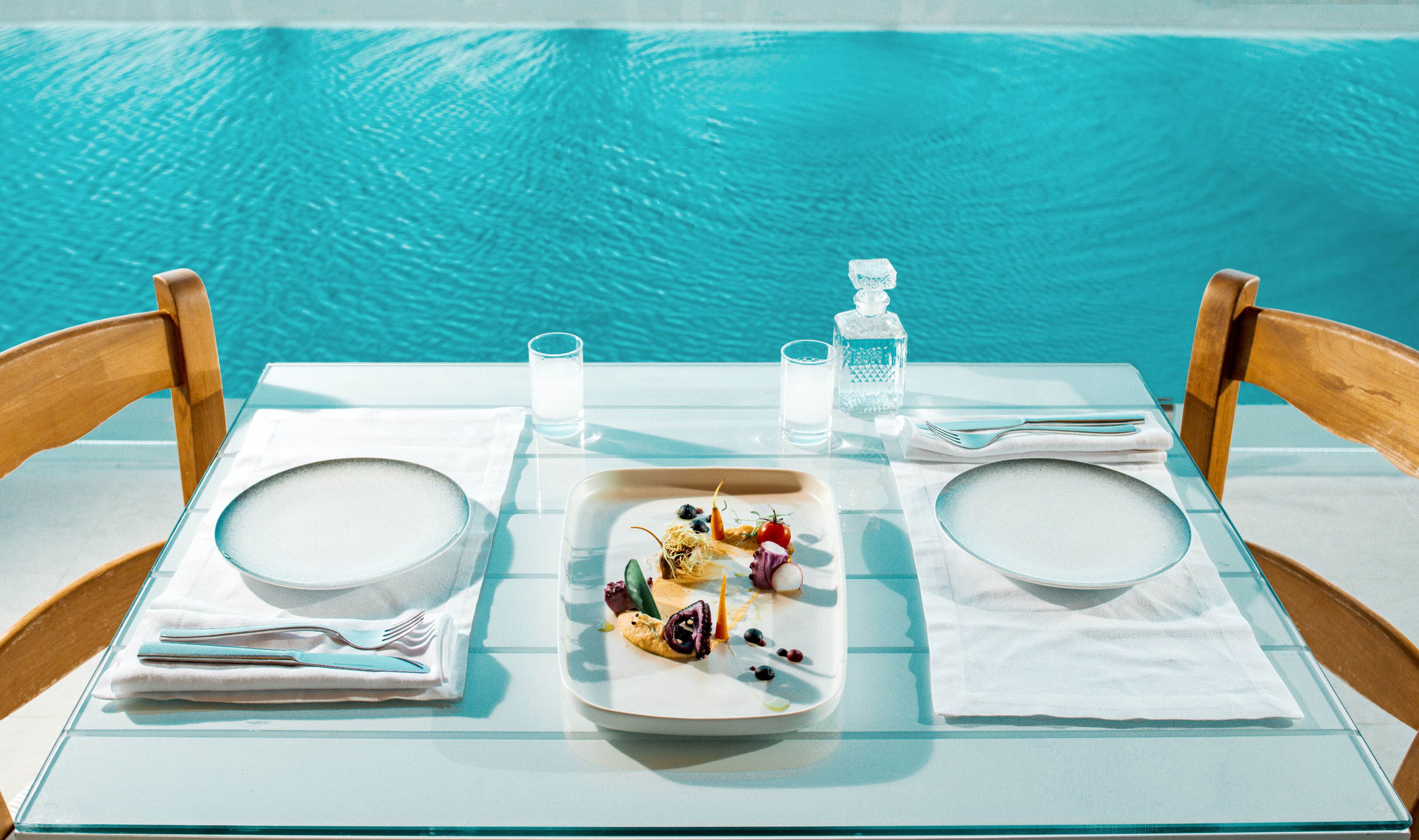 Ein Esstisch mit Tellern, Besteck und einem Glas Wasser am Pool.