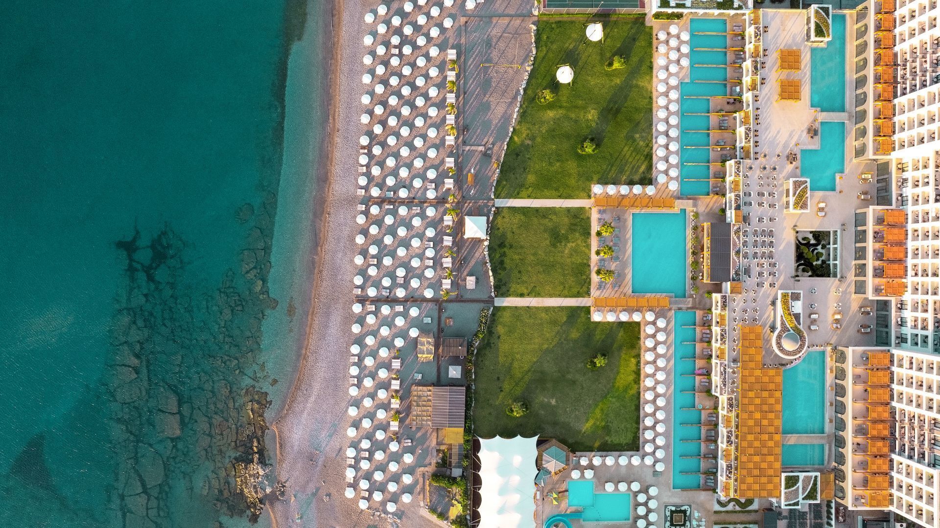 Vista aérea de un complejo turístico con playa, piscinas y tumbonas.