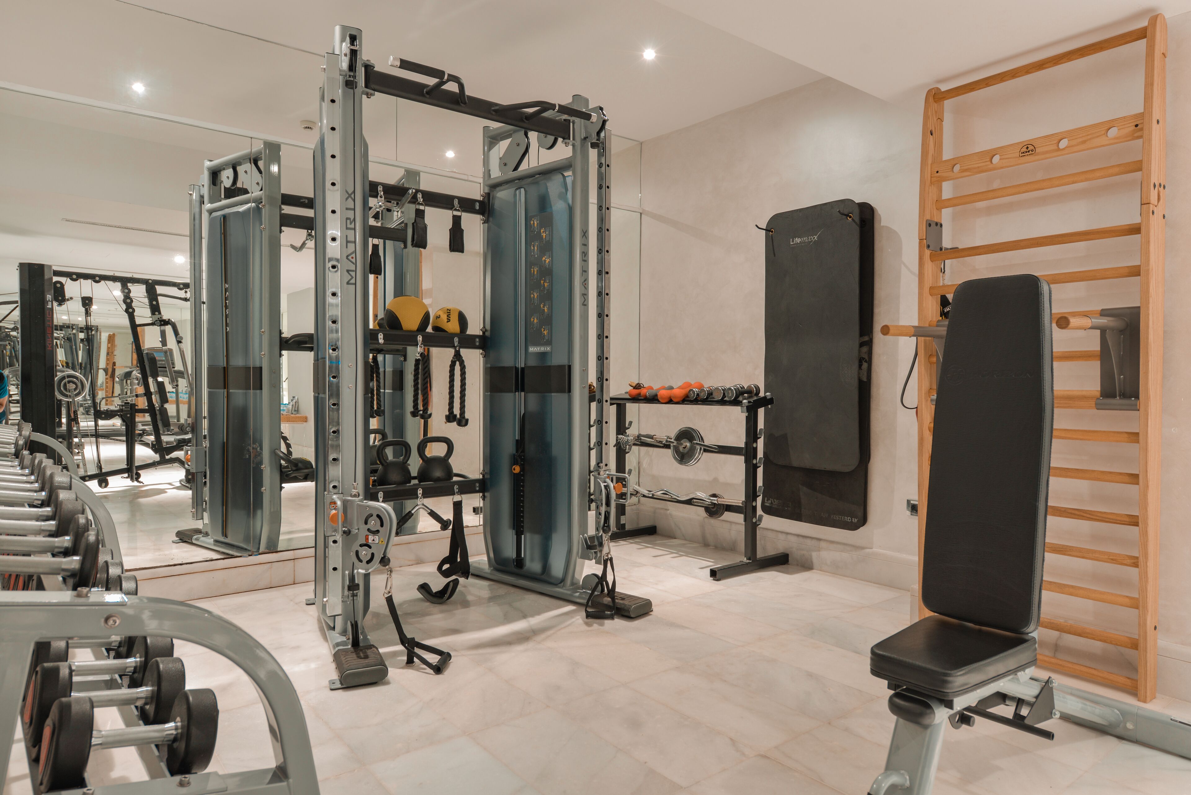 Een sportschool met diverse fitnessapparaten, waaronder een squatsrek, gewichtbank en losse gewichten.