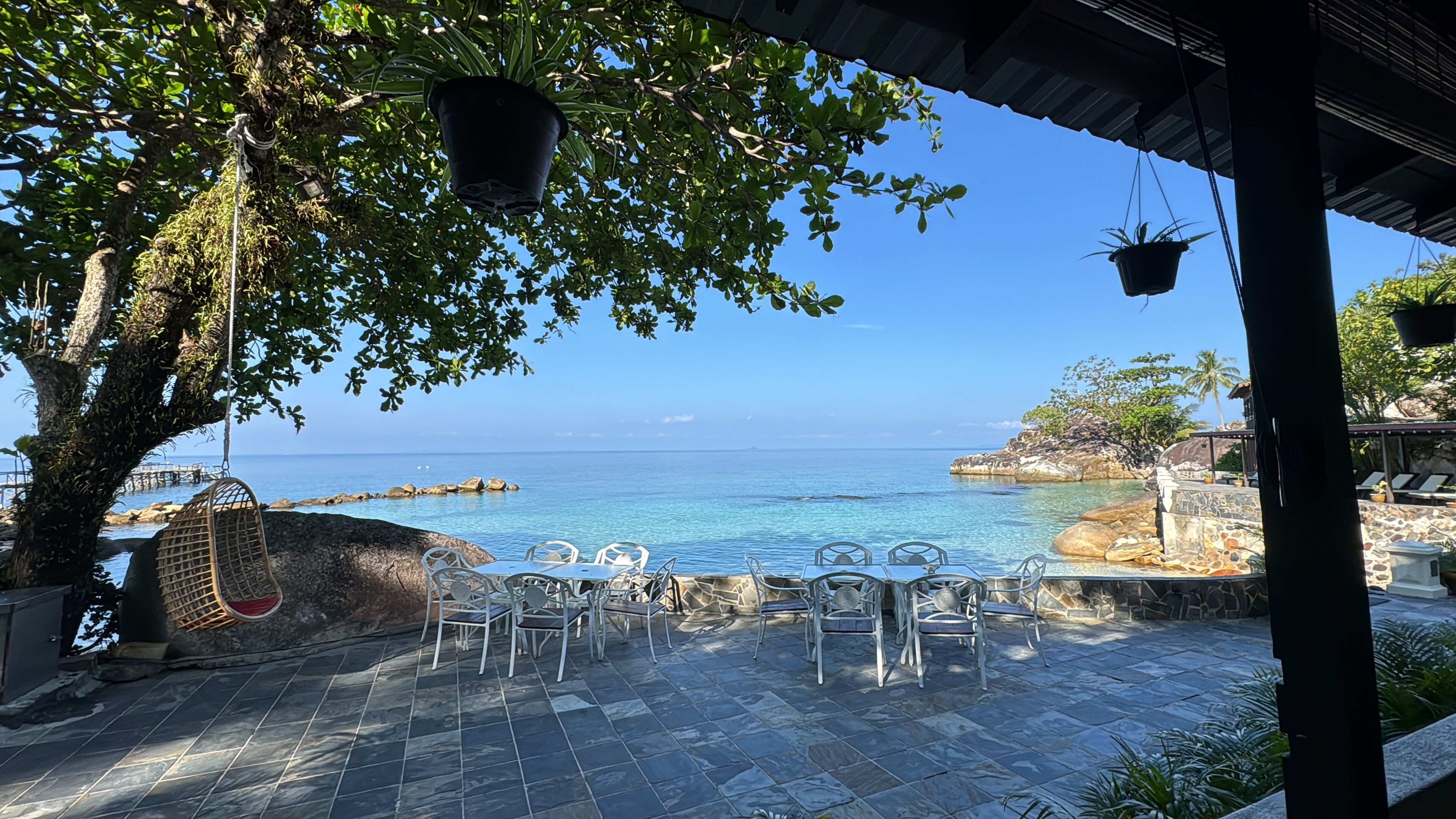 Un patio vista mare con pavimento in pietra, sedie in metallo e fioriere sospese.