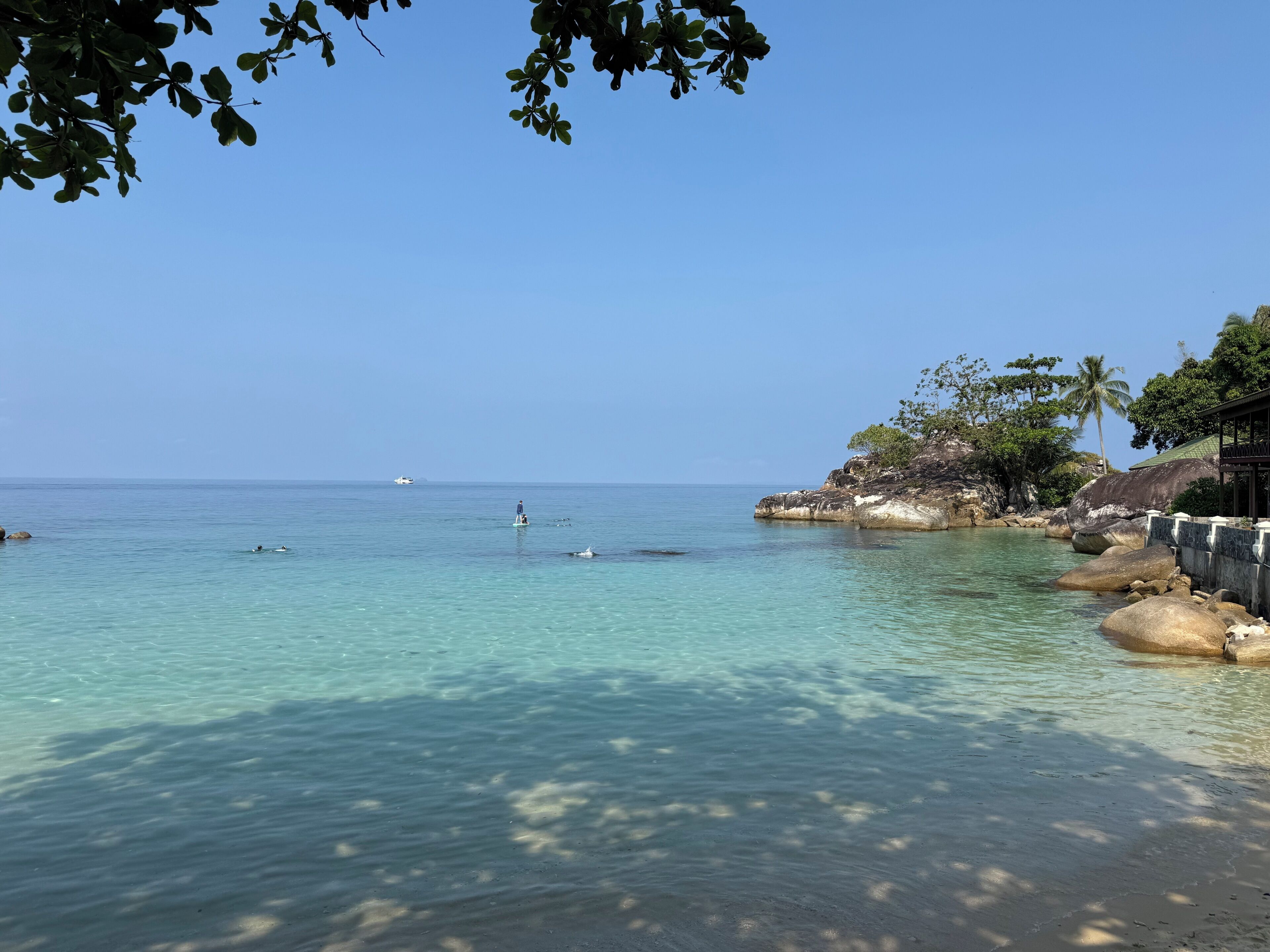 Un paysage côtier avec une eau claire, une côte rocheuse et un bâtiment doté d’un toit.