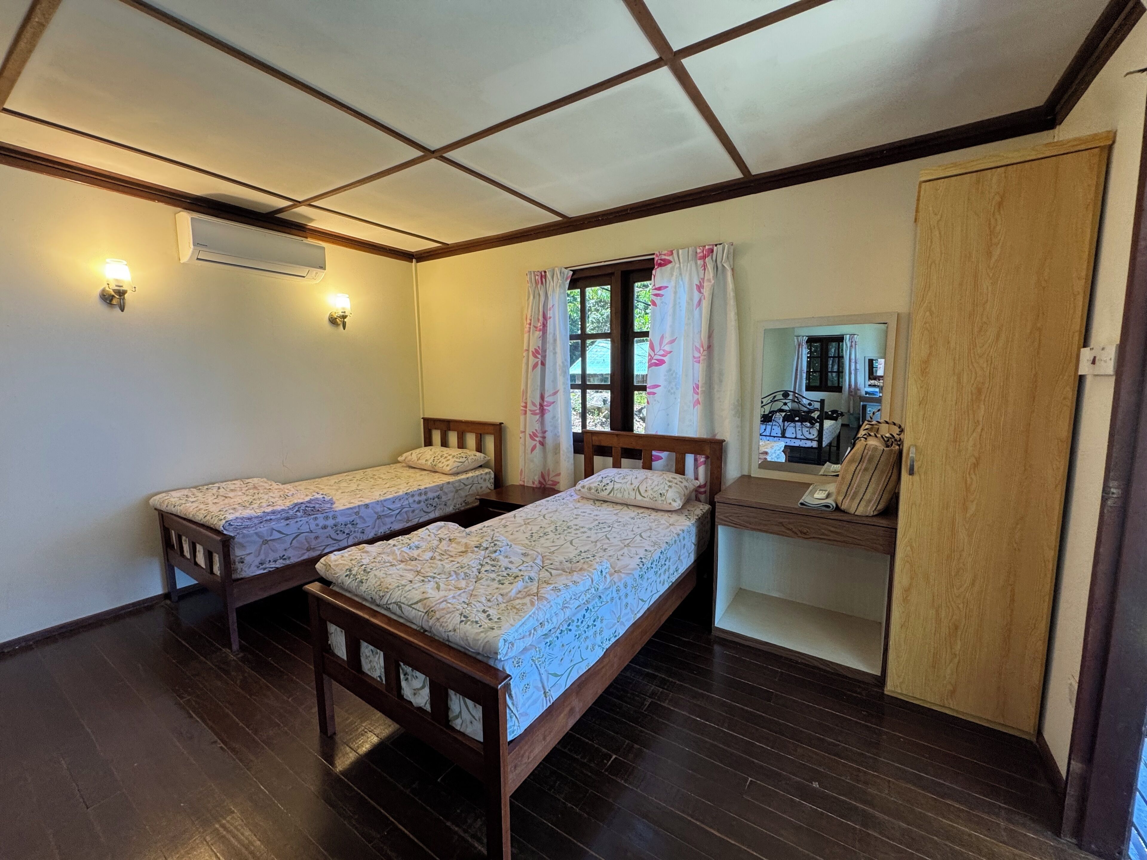 Een slaapkamer met twee houten bedden, een houten bureau, een spiegel en een airconditioning.