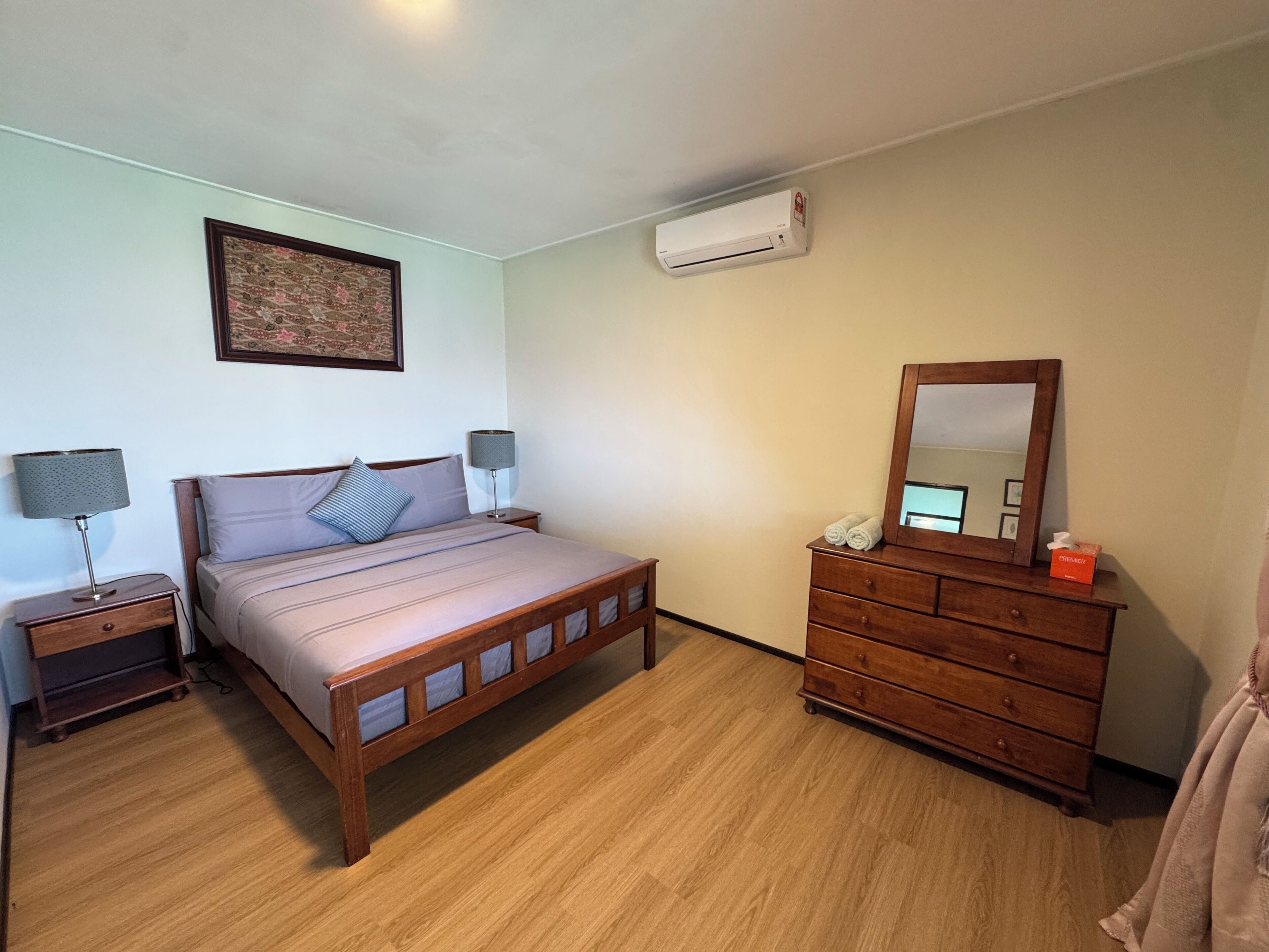 A bedroom with a bed, a dresser, a nightstand, a lamp, a mirror, and an air conditioning unit.