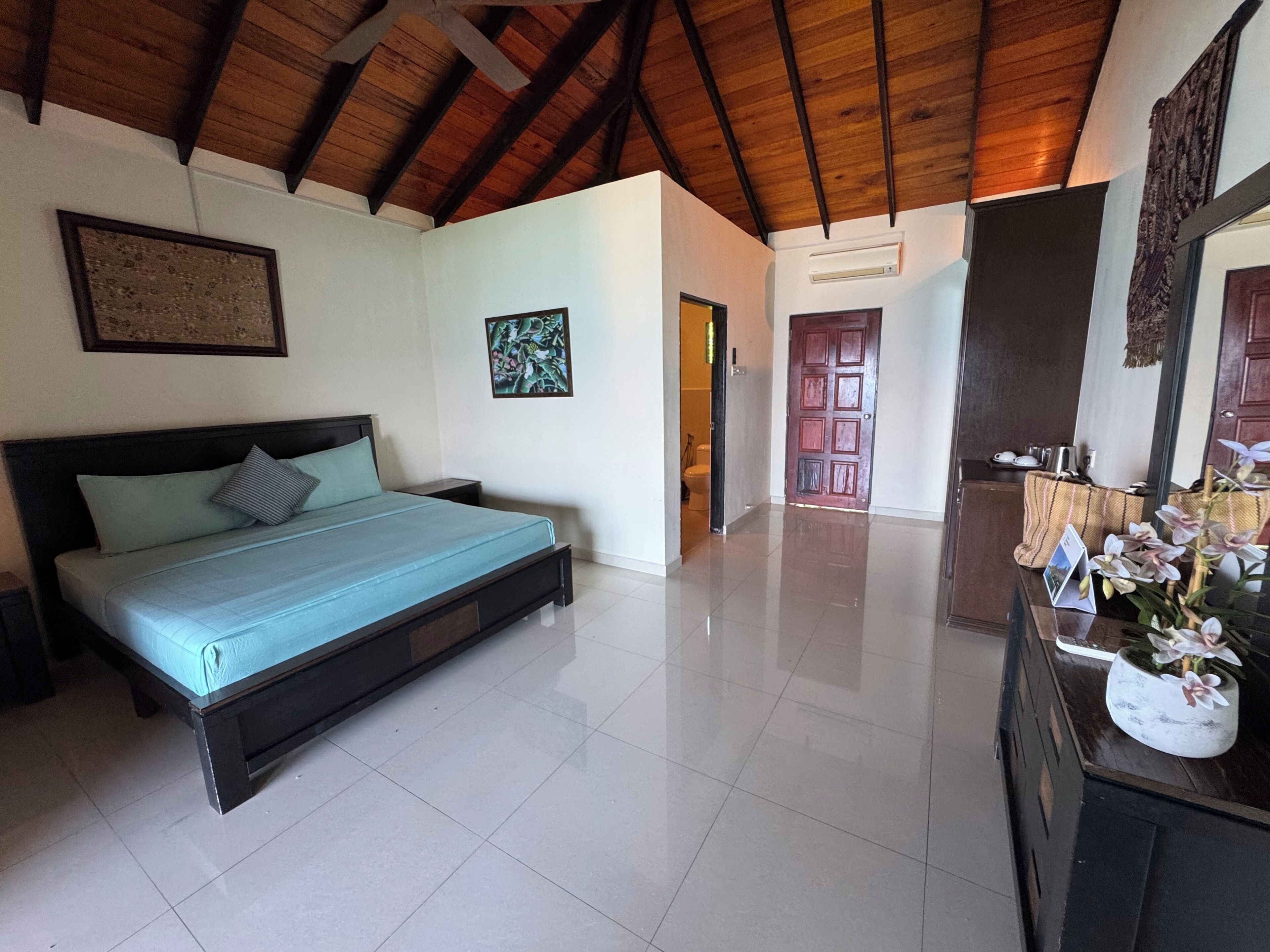A bedroom with a bed, a wooden ceiling, a door, and a mirror.