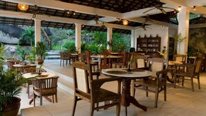 A spacious indoor dining area with wooden tables and chairs, surrounded by potted plants and a bookshelf. - Minang Cove Resort (Tioman Island)