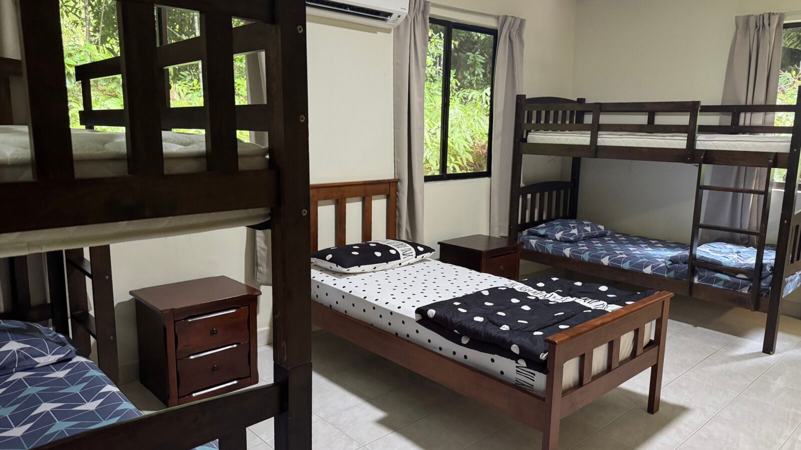 A dormitory room with bunk beds, a wooden desk, and a window with curtains.