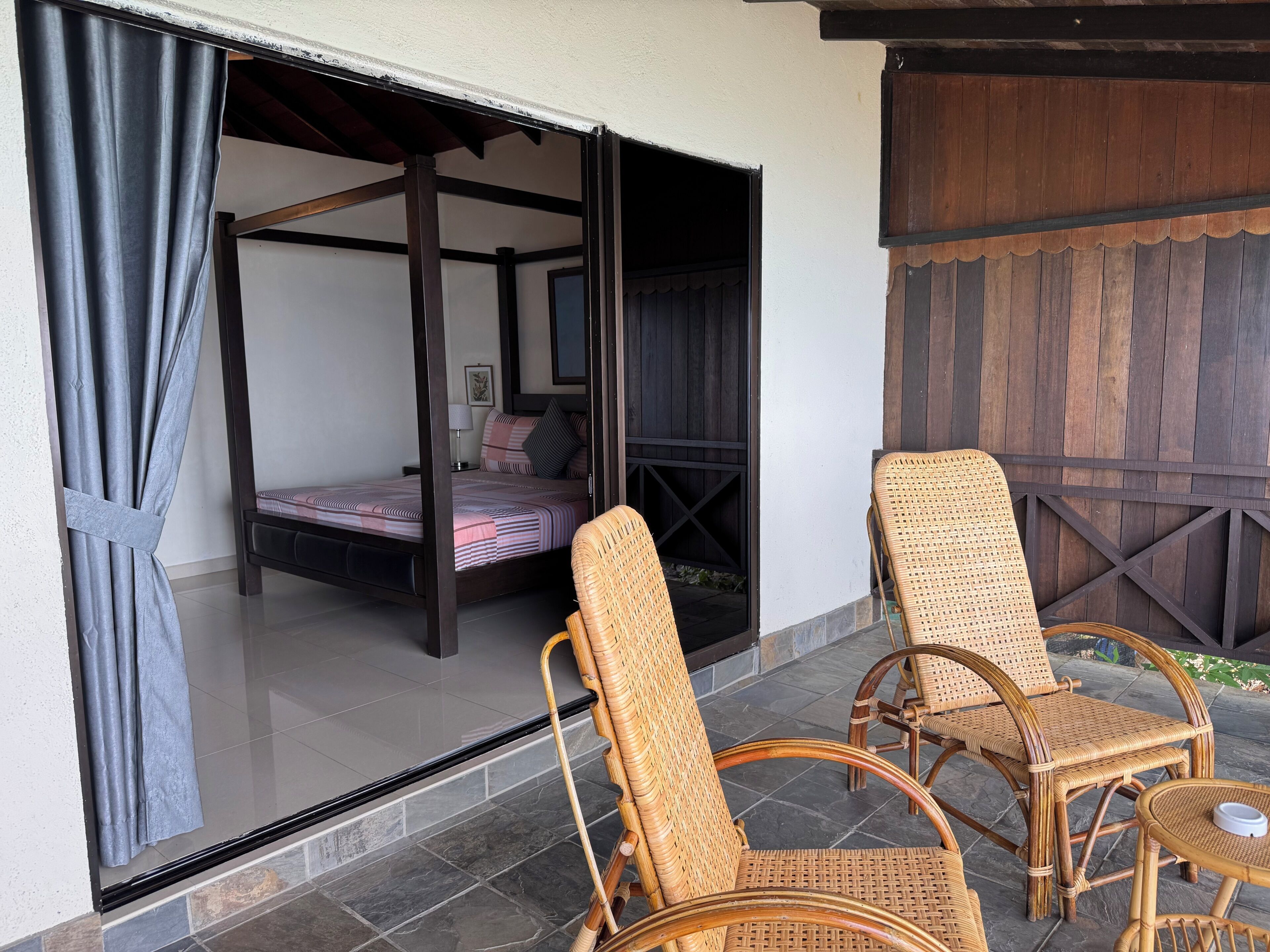 Una habitación con cama, ventana con cortinas y mobiliario de mimbre.