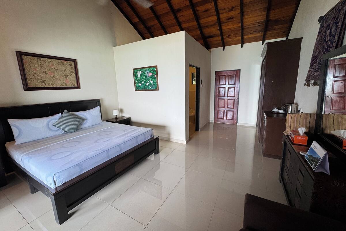A bedroom with a bed, a nightstand, a wooden ceiling, a door, and a dresser.