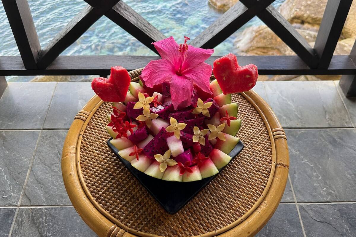 A tropical fruit and flower arrangement on a woven tray.