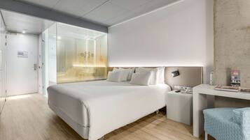 A modern hotel room with a large bed, bedside table, and a desk with a chair.