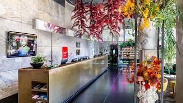 Een moderne receptie met een marmeren wand, een receptiebalie en een grote bloemenvaas.